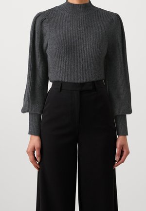 Grå ribstrikket sweater med puffede ballonærmer, kombineret med højtaljede sorte bukser med vide ben, vist fra hals til hofter.