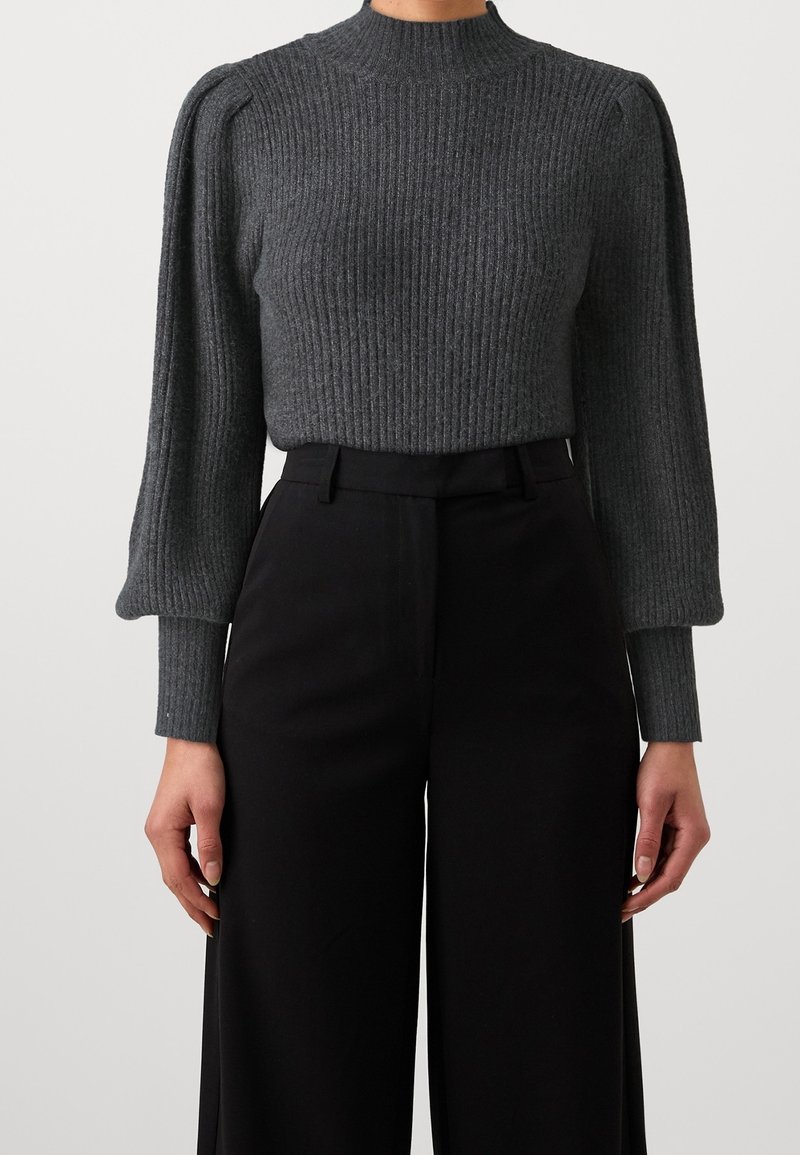Pull gris en maille côtelée avec des manches ballon bouffantes, associé à un pantalon noir taille haute à jambes larges, montré du cou aux hanches.