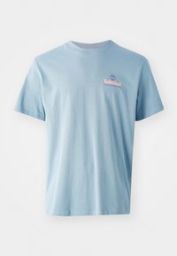 Camiseta de algodón azul claro con mangas cortas; presenta un pequeño logo de Timberland en color rosa y el texto "Boots With Roots" en el lado izquierdo del pecho.