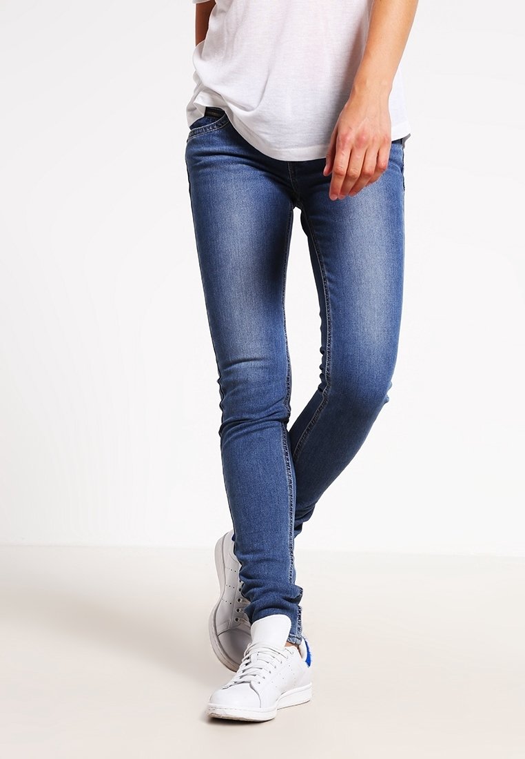 Úzké džíny ve střední modré barvě, s jemnou denimovou texturou a mírným odřením, doplněné bílými teniskami.