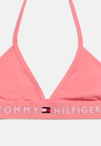 Ροζ τριγωνικό μπικίνι τοπ με μονόχρωμο σχέδιο, με λευκή ελαστική ταινία με λογότυπο μπροστά.