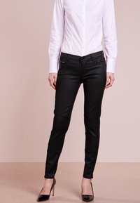 Svarta, slim-fit byxor med en slät textur, med dekorativa dragkedjor och panel sömnad. Kombinerade med en vit åtsittande skjorta och svarta klackar.