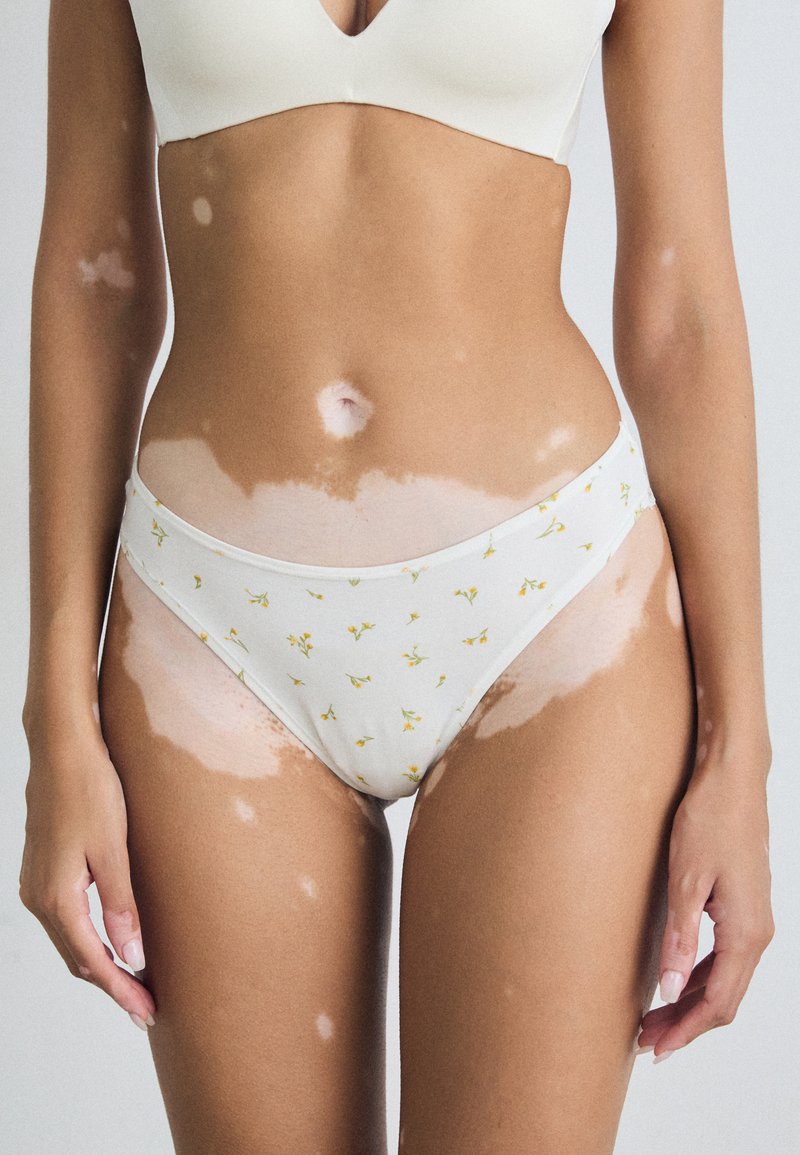 Pamučni bikini donji veš u bijeloj boji s malim žutim cvjetnim uzorkom. Mekani materijal, nisko rezani dizajn i glatka elastika.
