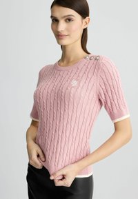 Roosa kudumine kahvli mustriga sviiter, lühikeste varrukatega ja kontrastsete valgete paeltega. Omab dekoratiivnuppe õlal ja logo broderi.