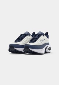 Nike Air tenisice s bijelim gornjim dijelom, tamnoplavi detalji, teksturiran materijal i vidljiva zračna amortizacija u potplatu.