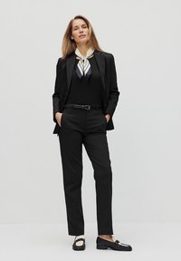 Zwarte maatpak met een op maat gemaakte blazer en rechte broek. Gecombineerd met een zwart top, een gestreepte sjaal en zwarte instappers.