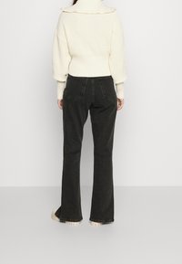 Knit cream sweater with a ribbed texture and ruffled collar, paired with black flared trousers featuring rear pockets and a raw hem.