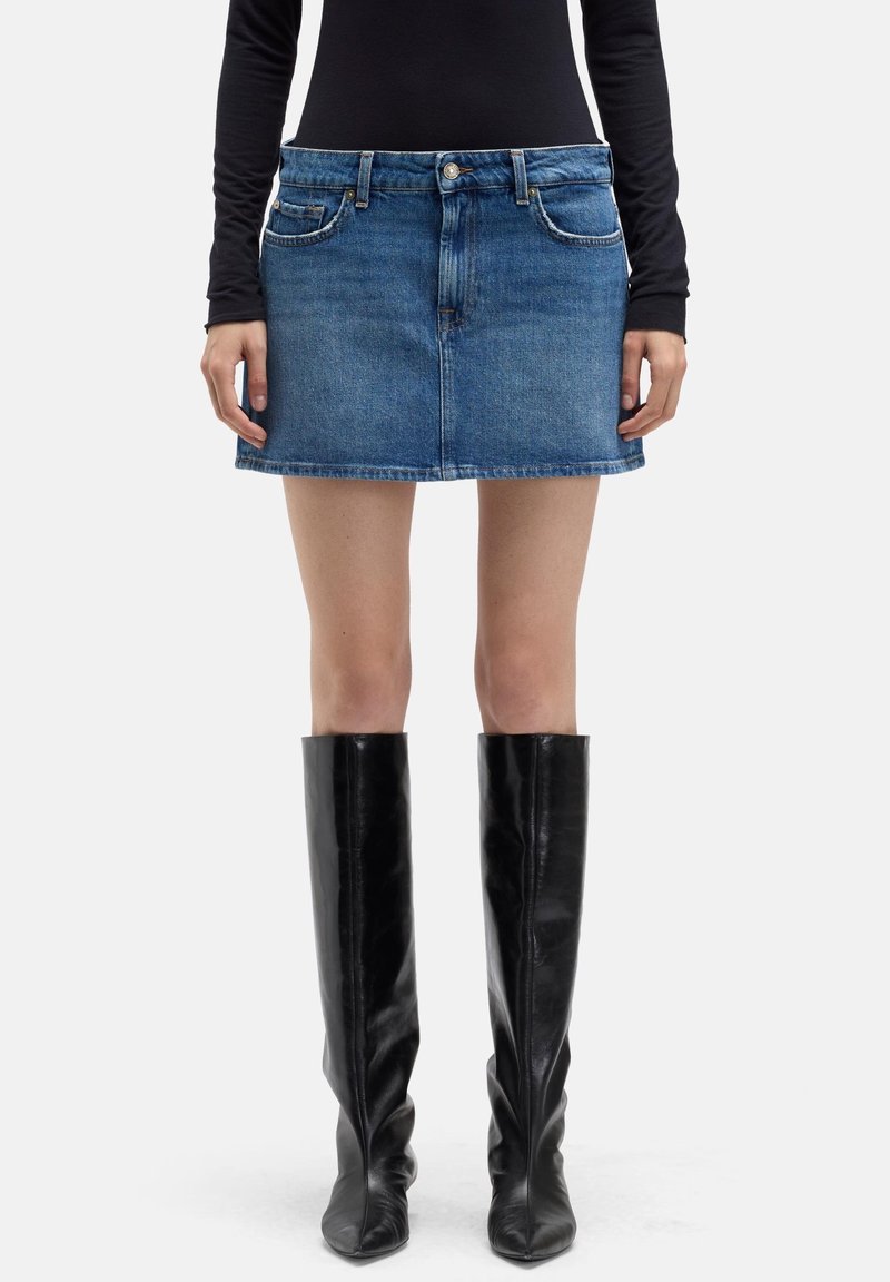 Jeans-Minirock in Blau mit klassischem Fünf-Taschen-Design, einem Bund mit Gürtelschlaufen und einem geraden Saum, kombiniert mit schwarzen Overknee-Lederstiefeln.