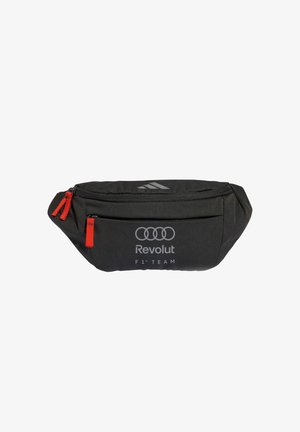Černá ledvinka s červenými přezkami na zip, která má logo kroužků Audi, nápis Revolut, značku F1 Team a jemné logo Adidas nahoře.