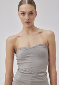 Top gris sin tirantes hecho de un tejido suave y elástico. Presenta una textura lisa y un escote curvado, que complementa la silueta ajustada.