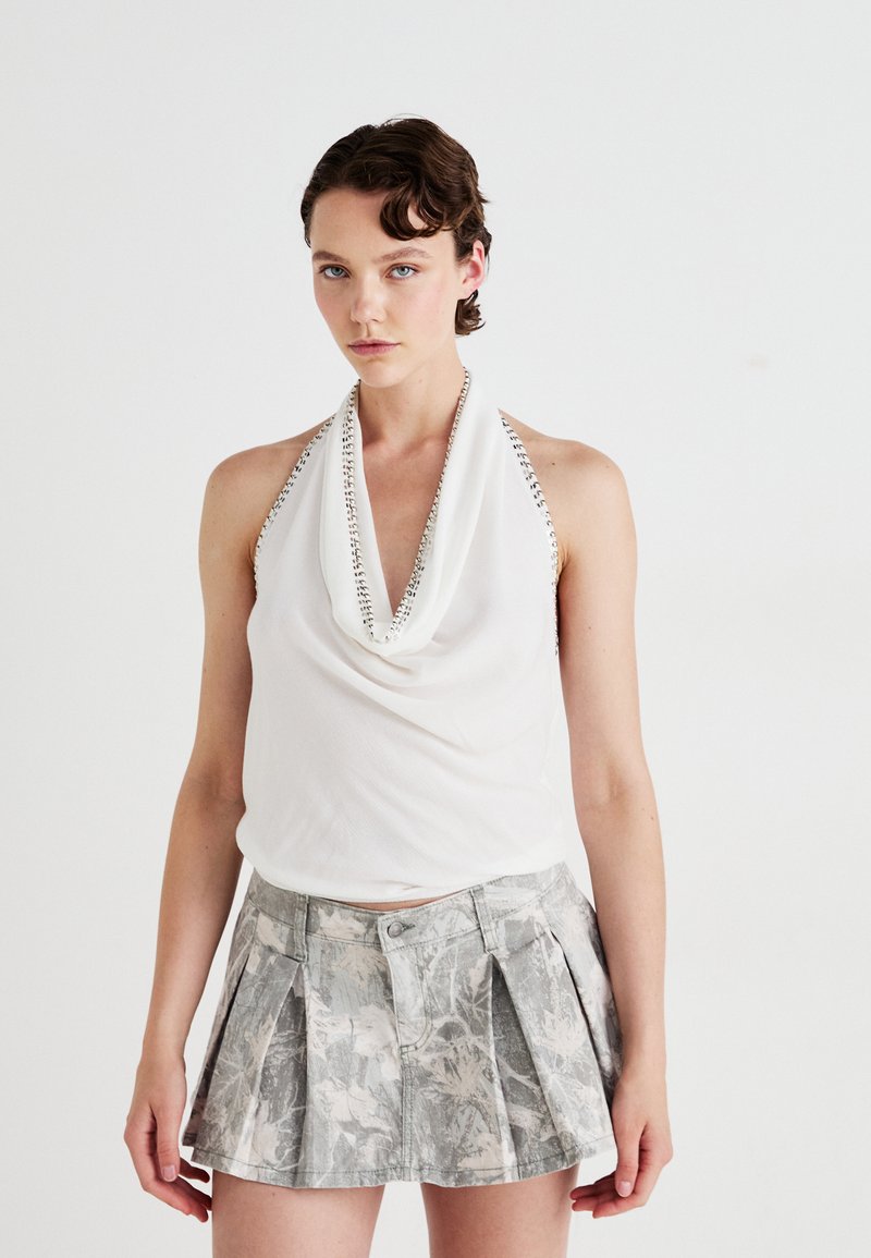 Top bianco con scollo drappeggiato e dettagli argento, abbinato a una mini gonna grigia con motivo, caratterizzata da pieghe e chiusura a bottoni.