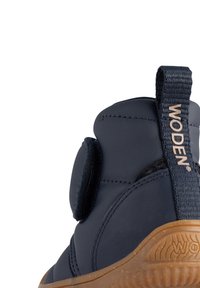 Navy blue ankle boot with a velcro strap, rubber sole, and embossed branding on the back. Smooth texture with a rounded shape.