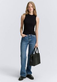 Top nero a coste senza maniche, con collo alto, abbinato a jeans blu svasati, borsa nera strutturata e scarpe nere con zeppa.