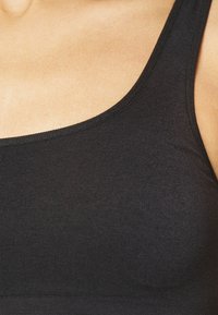 Top sin mangas de tela negra con escote redondeado. Material texturizado y elástico. Costuras limpias y un ajuste suave, adecuado para superposiciones.