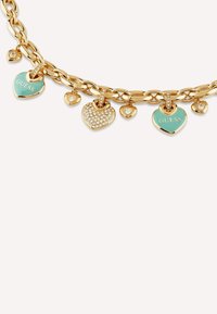 Bracelet en chaîne dorée avec plusieurs breloques en forme de cœur. Comprend un cœur turquoise avec "GUESS", un cœur orné de cristaux et des accents lisses.