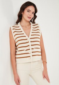 Crème en bruine gestreepte mouwloze gebreide cardigan met een diepe V-hals, vijf parelknopen en zijzakken. Gladde textuur.