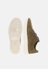 Baskets en daim marron avec semelle blanche, lacets gris et motif de semelle détaillé, vues de côté et de dessous sur un fond clair.