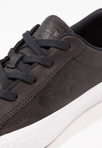 Sneaker in pelle nera con superficie texturizzata, dotato di lacci neri, suola in gomma bianca e dettaglio a stella in rilievo sul lato.