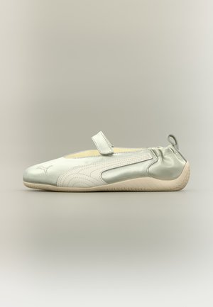 Zapato sencillo gris claro tipo slip-on con tira de velcro, suela flexible, lengüeta para tirar en el talón y logo Puma cosido en la puntera.