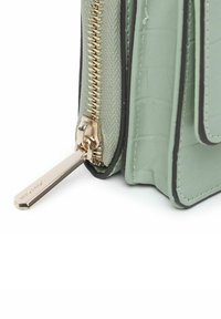 Zielona torebka z ekoskóry o fakturze krokodylej, z złotym zamkiem błyskawicznym i czarnymi akcentami na brzegach. Zamek błyskawiczny ma subtelny detal z logo.