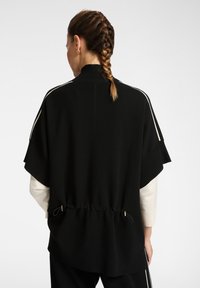Czarny oversize sweter z półgolfem, krótkimi rękawami, regulowanym sznurkiem w talii oraz białymi paskami po bokach.