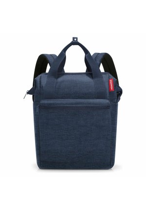 Marineblauer quadratischer Rucksack mit gepolsterten Trägern, zwei oberen Griffen, Vorderfach mit Reißverschluss und rotem Markenschild an der Seite.