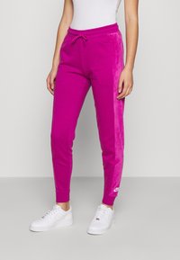 Rosa sweatpants med en texturerad rand längs sidan, dragsko i midjan, elastiska muddar och vitt Nike-logotyp på det nedre benet.
