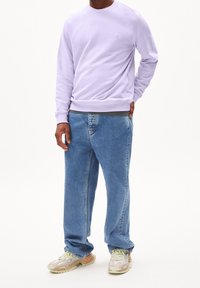 Ljuslila sweatshirt med rund halsringning, lös passform, kombinerad med blå raka jeans. Skorna är mångfärgade med texturerad design.