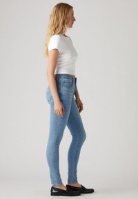 Los jeans de denim azul ajustados presentan una cintura alta y una textura suave. Combinados con una camiseta blanca ajustada y mocasines negros.