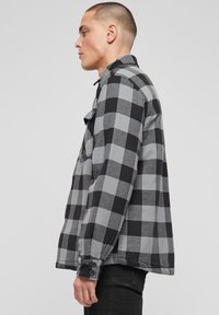 Pilko ir juodo languoto flanelinio audinio marškiniai su ilgomis rankovėmis, užsegamais rankogaliais ir viena krūtinės kišene, pasižymintys laisva forma ir minkšta tekstūra.