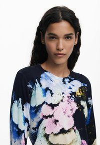 Lightweight sweater featuring a dark background with vivid floral patterns in pink, blue, and yellow. Crew neckline and textured knit design.