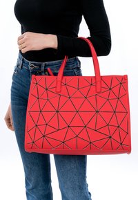 Borsa tote con motivo geometrico rosso e accenti triangolari neri, realizzata in materiale sintetico liscio, dotata di due manici robusti.