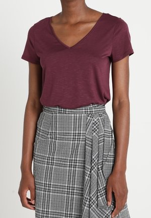 T-shirt bordeaux à col en V associée à une jupe taille haute à carreaux noir et blanc, dotée d'un design portefeuille et de plis.