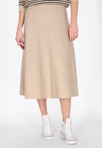 Jupe évasée beige en tissu texturé, atteignant le mollet. Associée à des baskets montantes blanches pour un look décontracté.