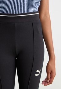 Čierne športové legíny s priliehavým strihom, s textúrovaným pásom, bielym pruhom a malým bielym logom Puma na boku.