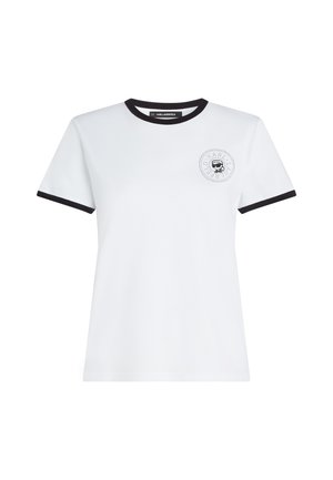 T-shirt blanc à manches courtes avec bordure noire au col et aux manches, présentant un petit logo circulaire avec une silhouette stylisée sur la poitrine gauche.