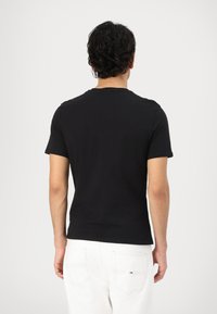 Camiseta negra de manga corta con cuello redondo, hecha de una tela suave, que presenta un diseño limpio. La parte trasera muestra una construcción simple, sin adornos.