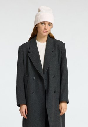 Cappotto in lana grigio a doppio petto con ampi risvolti e due bottoni, abbinato a un berretto di lana spesso color crema. Texture liscia, vestibilità casual.