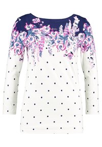 Bloemrijk langarmshirt met een witte hals, marineblauwe stippen en marineblauwe schouders. Heeft een multicolore bloemenpatroon over het borstgedeelte.
