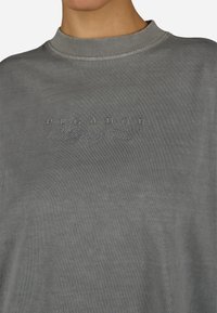 Hallitusehall sweatshird, millel on sooniline ümar kaelus, esiküljel on toonaalne tikand "PEGADOR" ja "Whispers of Cold". Pehme tekstuur.