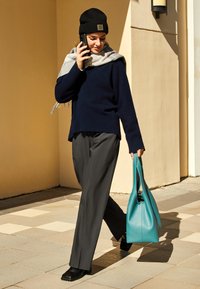 Granatowy wełniany sweter, szary szalik, szare spodnie, czarne buty i turkusowa skórzana torebka, spacerująca po płytkach na tle beżowej ściany.