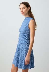 Blauwe jurk met witte stippen, aansluitende top met hoge halslijn, mouwloos ontwerp en uitlopende rok. Soepele textuur, casual stijl.