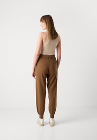 Pantaloni marroni in maglia con un design a gamba affusolata e polsini elastici, abbinati a una canotta beige; modello in piedi leggermente di lato.