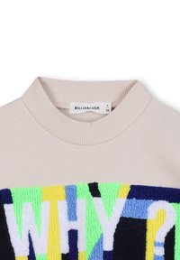 Sweatshirt in een lichte beige kleur, met een ribbelachtige halslijn en een textuurdesign met "WAAROM?" in levendige kleuren: groen, geel, blauw en zwart.