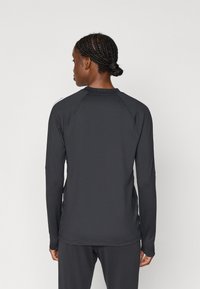 Μακρυμάνικη μπλούζα σε σκούρο γκρίζο ύφασμα με λεία υφή. Διαθέτει στρογγυλή λαιμόκοψη και ράγλάν μανίκια, σχεδιασμένη για αθλητική χρήση.