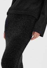 Black outfit featuring a textured, fuzzy fabric skirt and a smooth, slightly shiny long-sleeve top, both in dark shades.