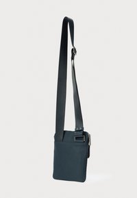 Mala tamnoplava torbica preko tijela s podesivim remenom i srebrnim patentnim zatvaračem na čistoj bijeloj pozadini.