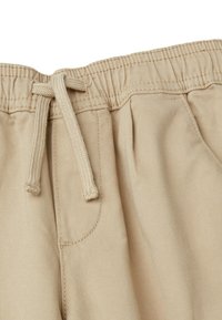 Pantaloni corti beige in cotone con vita elastica, cordino regolabile e tasca laterale. Texture liscia e design semplice.