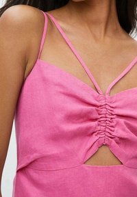 Top de lino rosa con tirantes finos, detalle fruncido en el frente y un corte abierto en la cintura. Textura suave y ajuste relajado.