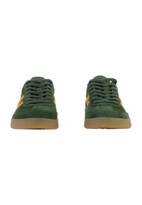 Green suede sneakers with yellow accents, textured laces, and gum rubber soles. Classic design with rounded toe and low profile.
